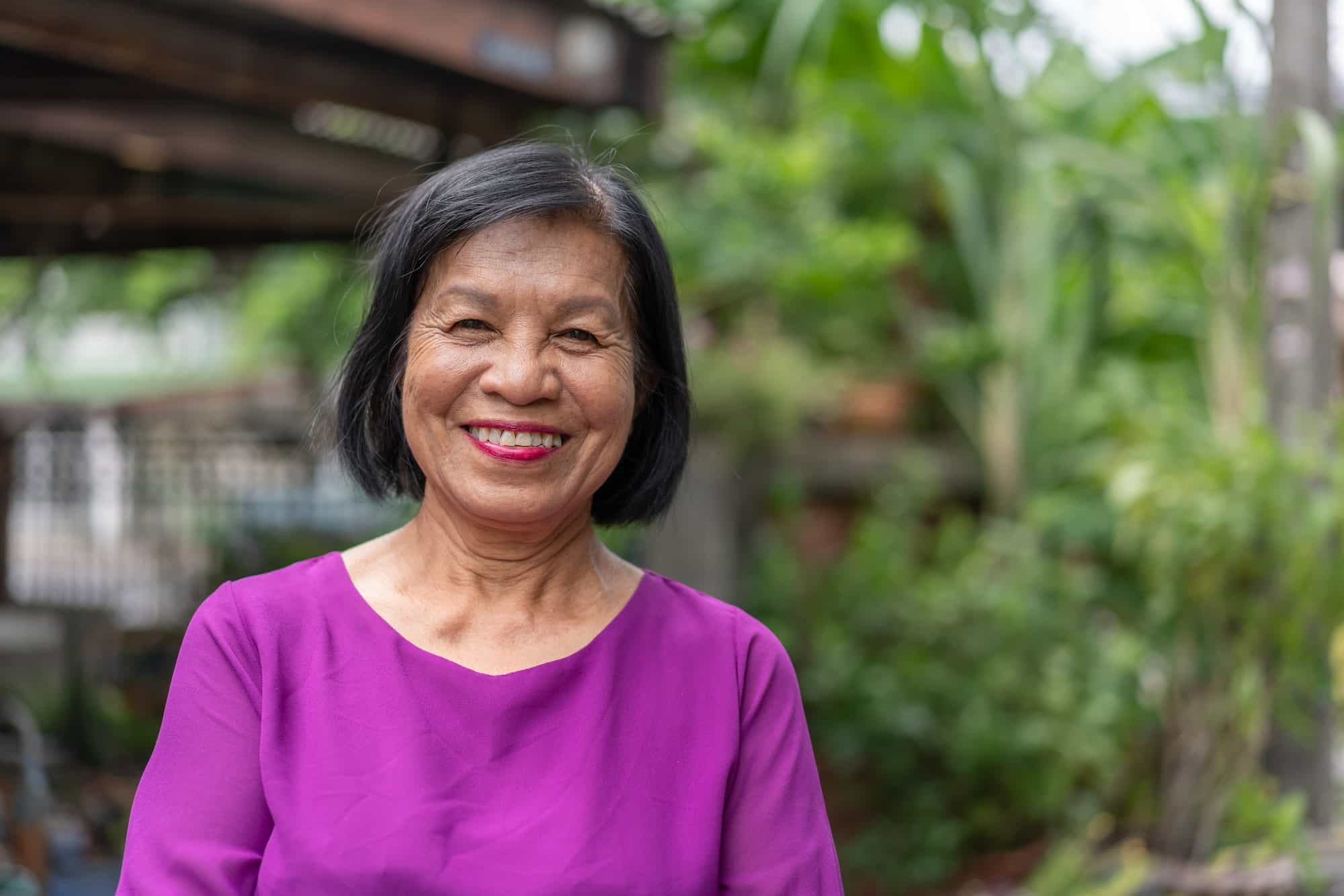 Smiling Asian elderly woman look at camera standing posing outside at home
