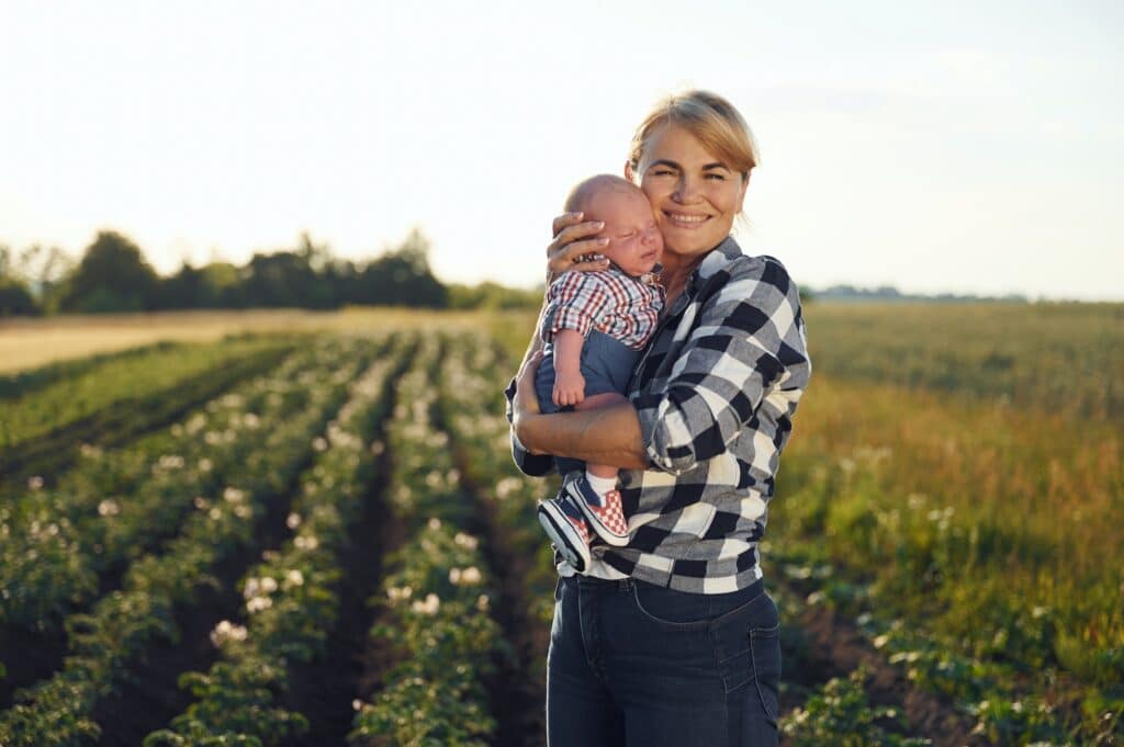 Standing and smiling, Happy woman on the agricultural field is with little baby in the hands