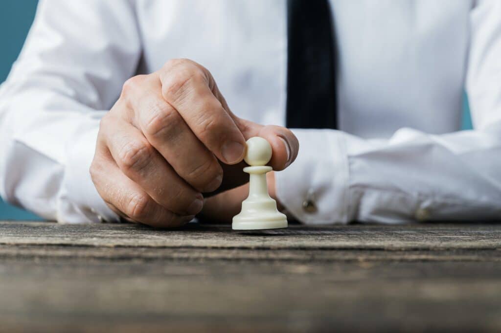 Businessman placing white pawn chess piece on wooden desk