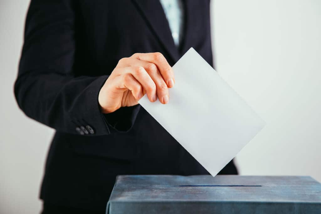 Close-up of voter putting ballot into voting box.