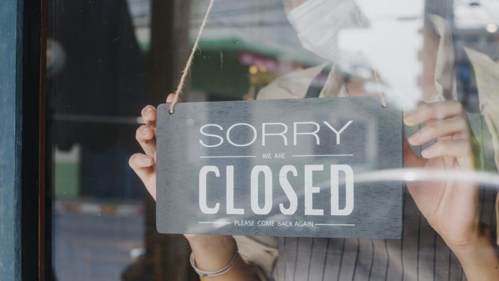 Young Asia girl wear face mask turning a sign from open to closed sign on glass door cafe