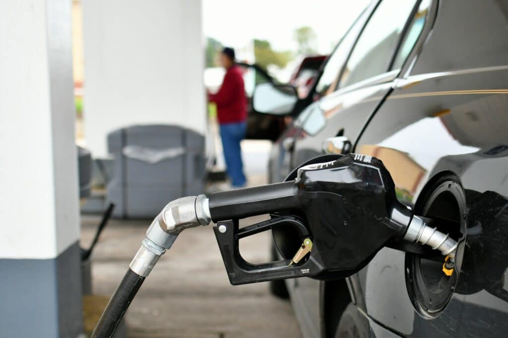 A gasoline pump handle in a gas tank of vehicle with another customer at gas pump in background